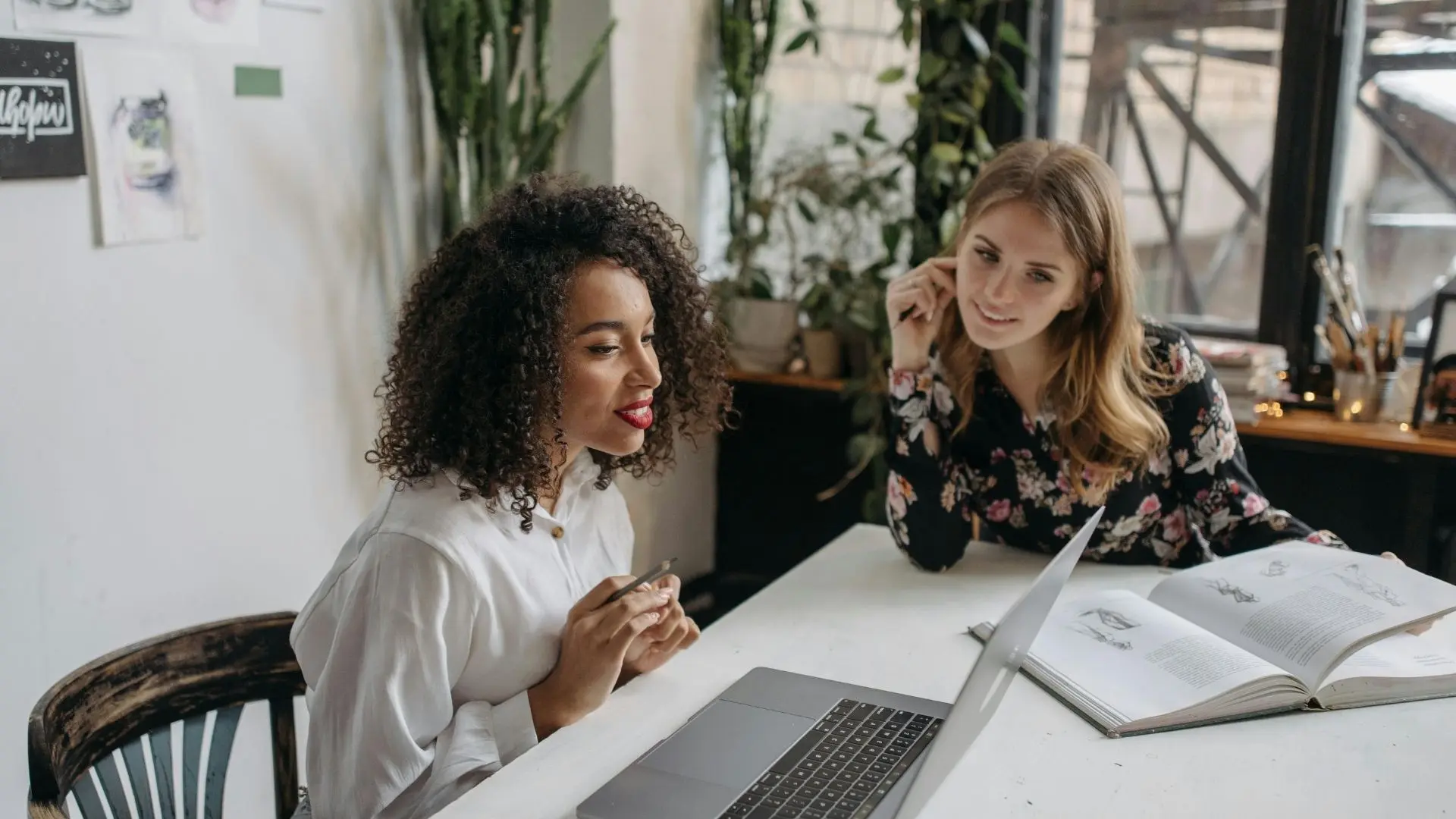 Two women who met in an online community for business owners, sitting at a white table working