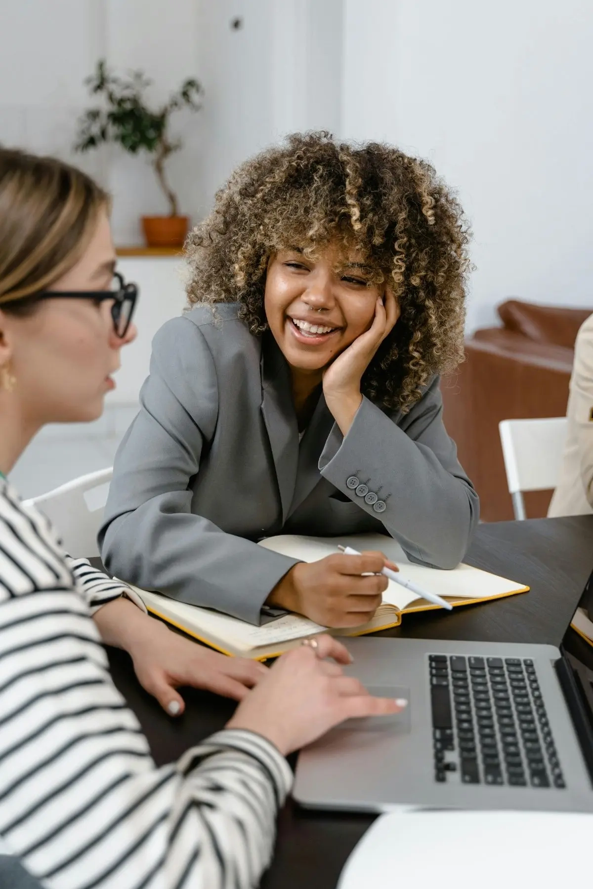 A women in a gray blazer smiling at another female business owner looking at her laptop