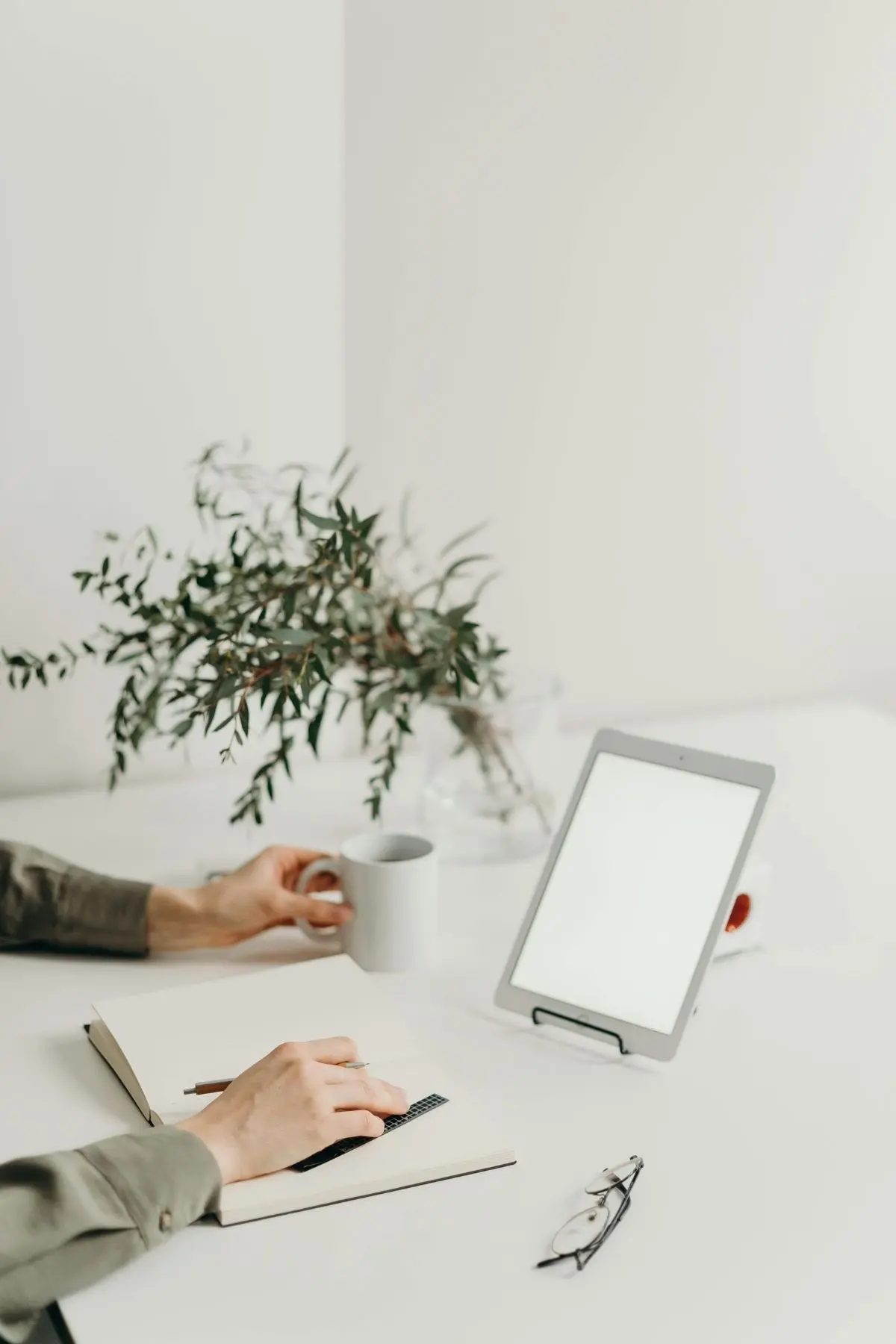 A laptop on a white desk with a plant and the arms of a female entrepreneur holding a coffee mug