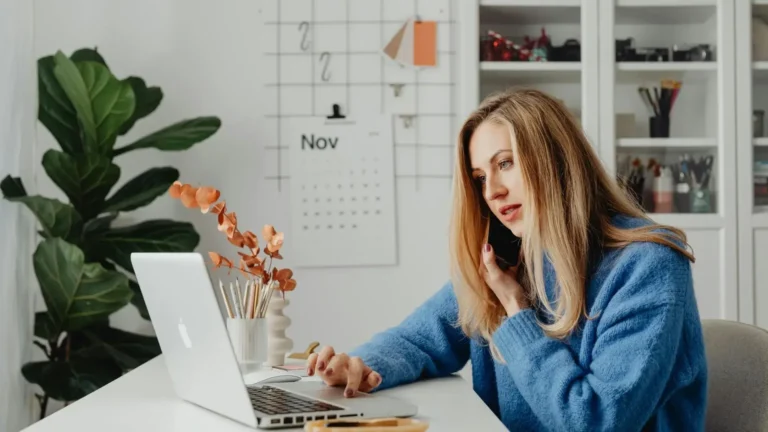 A female entrepreneur in a blue jacket talking on the phone and looking at her laptop